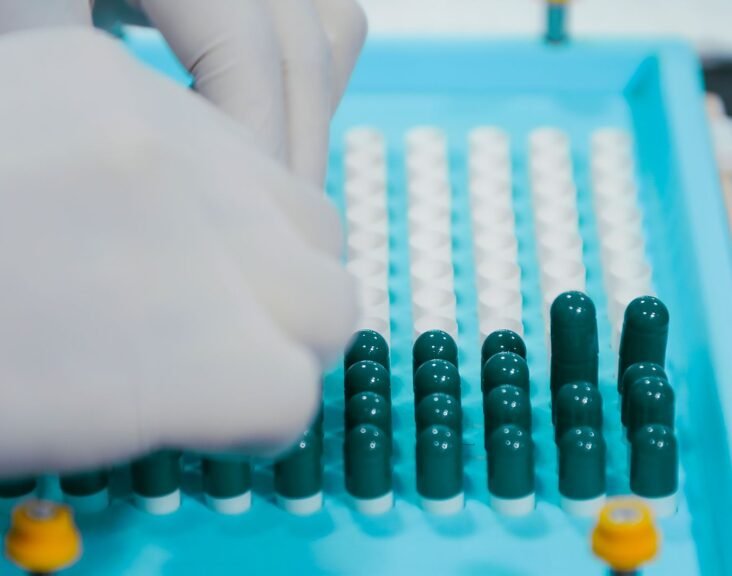 Gloved hands arranging capsules on a pharmaceutical production tray, representing Indian generic drug manufacturing