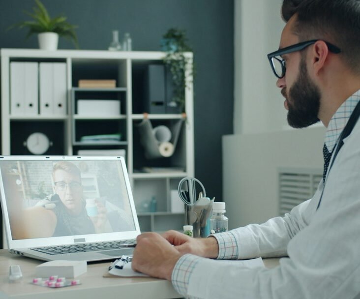 Doctor in white coat engaging in a digital video consultation on a laptop, representing omnichannel HCP engagement in pharma