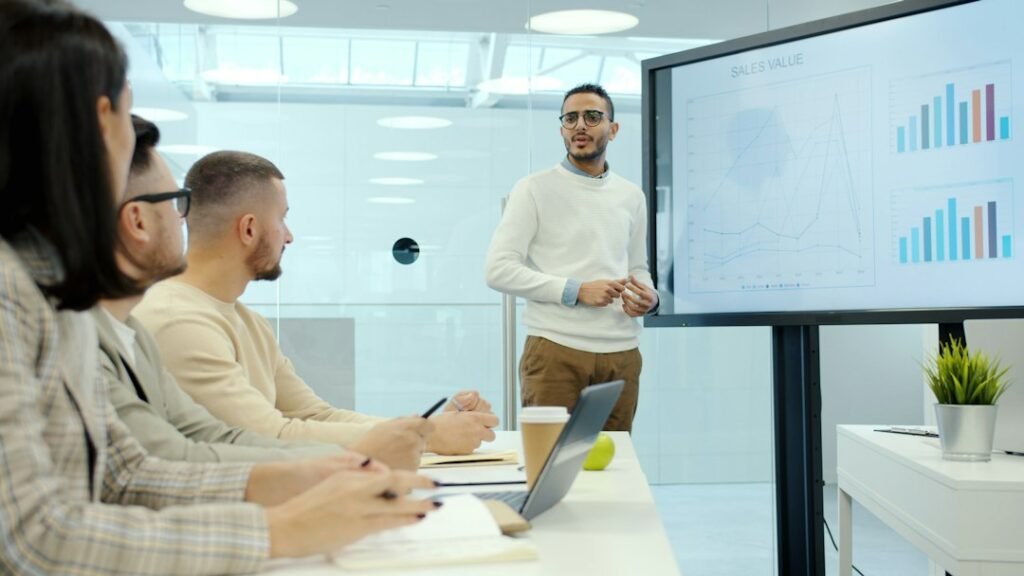 Sales team training session with presenter showing data charts on a digital screen — illustrating structured pharma MR onboarding curriculum delivery